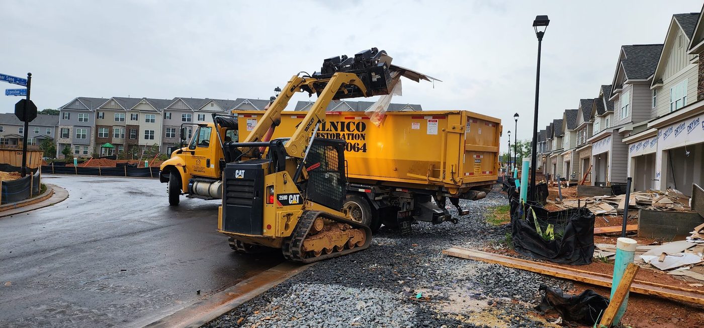 CAT skid steer dumping debris into Alnico container at townhome site
